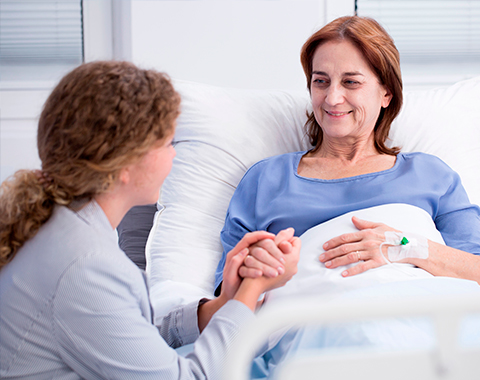 Mulher internada em hospital sorrindo enquanto conversa com uma acompanhante.